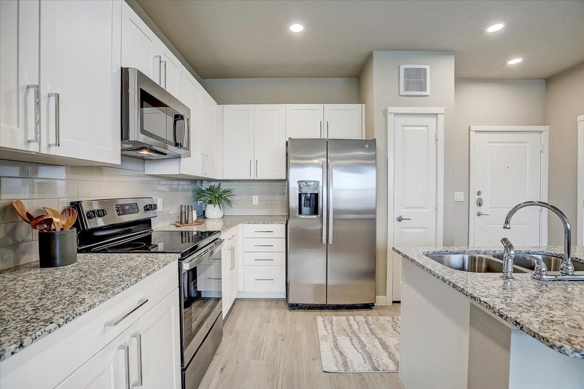 White-cabinet kitchen with granite counters, subway tile backsplash, and stainless refrigerator, range, and microwave.